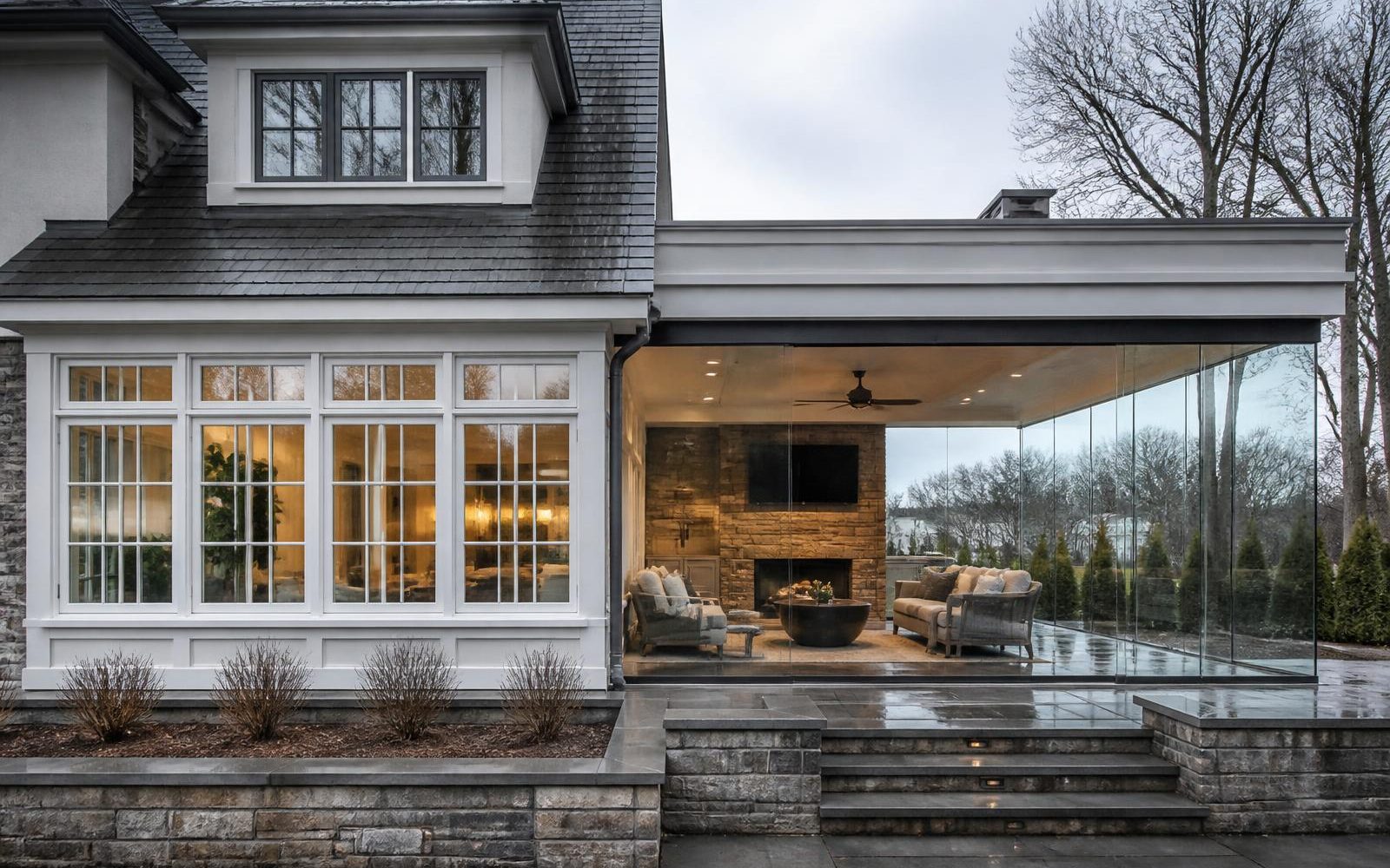 A home showing a traditional white-framed sunroom next to an open frameless glass enclosure for direct comparison